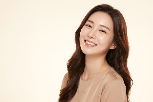 นางแบบหญิงเอียงศีรษะและยิ้มสดใส ท่ามกลางพื้นหลังสีงาช้างอ่อน