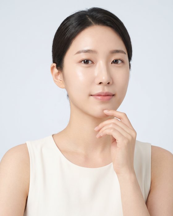 회청색 배경 앞에서 손끝을 턱에 대고 정면을 바라보는 여성 모델