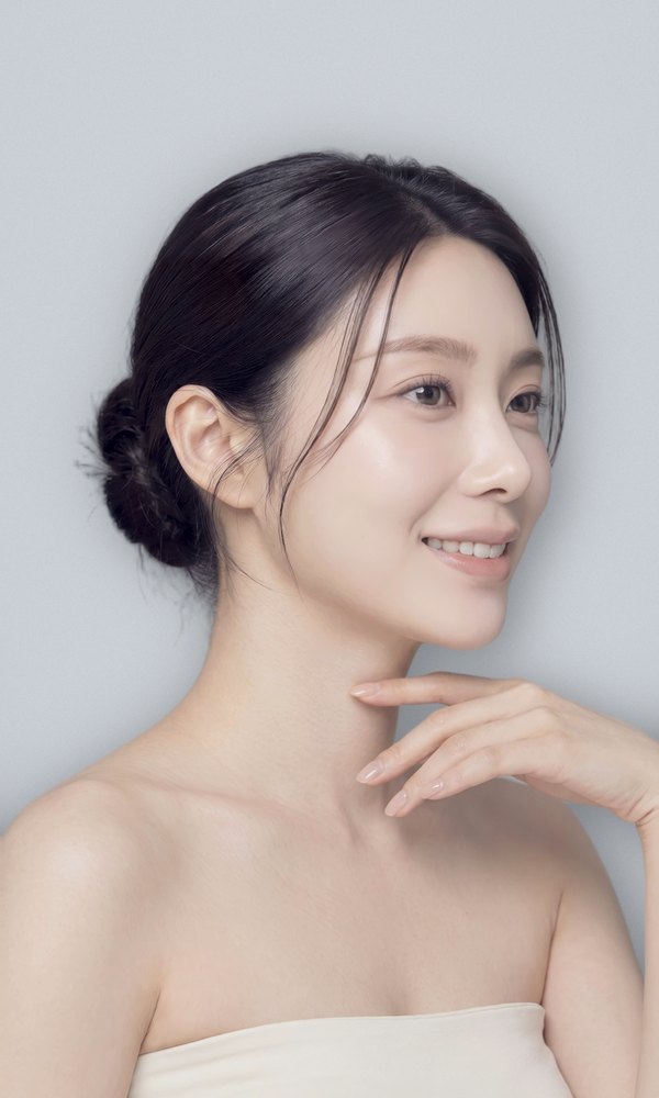 Revision eye and nose surgery signature shot — female model with her hair tied low, looking to the side