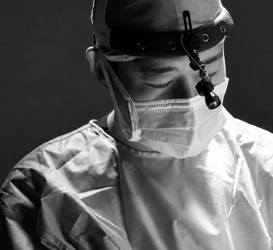 Plastic surgeon in surgical attire and magnifying loupes, focused on the operation