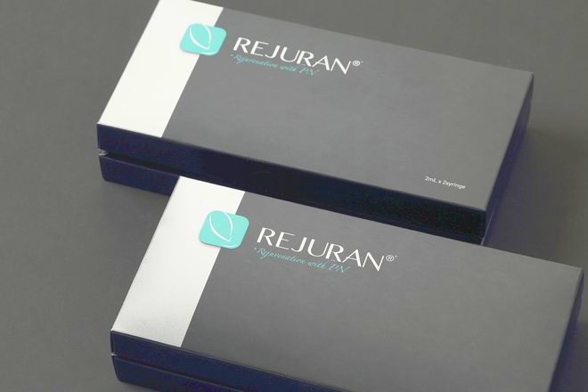 Dua kotak produk Rejuran Healer diletakkan miring di atas latar abu-abu